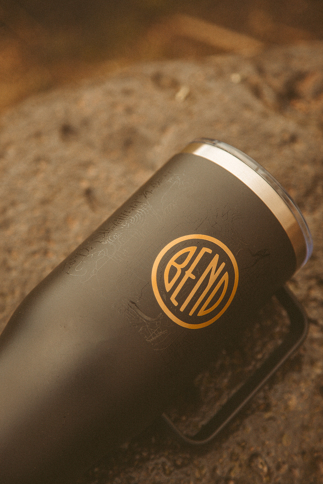 Close-up of a black stainless steel tumbler with a goldCity of Bend logo against a typographic map.